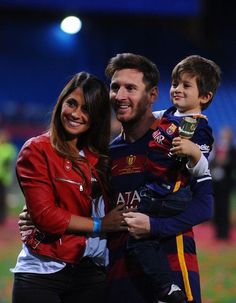 a man and woman holding a small boy in their arms while standing on a soccer field