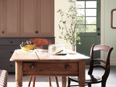 a wooden table sitting in front of a window next to a chair and cabinet with drawers