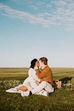 a man and woman sitting on the grass kissing