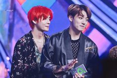 two young men standing next to each other holding an award in front of a colorful background