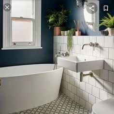 a white bath tub sitting under a bathroom window next to a toilet and sink in a bathroom