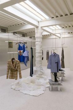 clothes are hanging on racks in an open space with white carpet and metal rails holding clothing