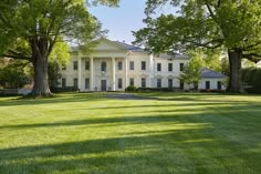 a large white house sitting on top of a lush green field next to tall trees