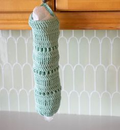 a crocheted bottle cover hanging from a kitchen cabinet door handle on a hook