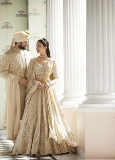 two people standing next to each other in formal wear, one wearing a white and gold outfit