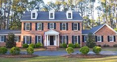 a large brick house with black shutters and white trim on the front door is surrounded by trees