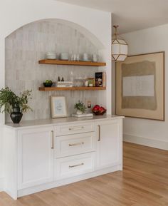 a kitchen with white cabinets and shelves filled with dishes on top of wooden flooring