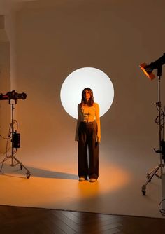 a woman standing in front of a light with two lights behind her and one lamp on the floor