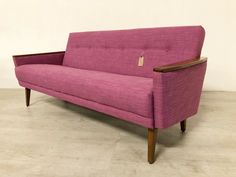 a pink couch sitting on top of a hard wood floor next to a white wall