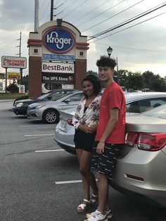 a man and woman standing next to each other in front of a car dealership