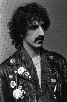 a black and white photo of a man wearing a leather jacket with patches on it