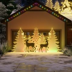 lighted christmas trees and deers in front of a garage with lights on the doors