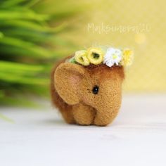 an elephant with flowers on its head sitting next to some grass and plants in the background