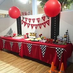 a red table topped with lots of cake next to orange cones and balloons on top of a hard wood floor