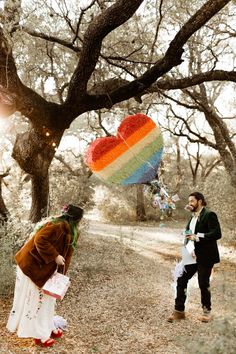 a man standing next to a woman under a tree with a rainbow heart shaped kite