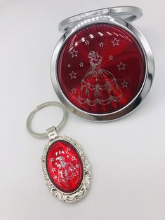 a compact mirror and keychain sitting on a white surface, with the image of a woman in a red dress