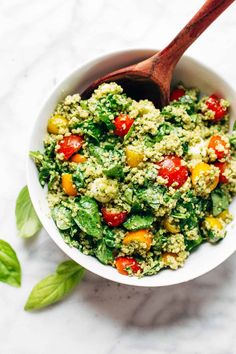 a white bowl filled with green and red food next to a wooden spoon on top of a marble surface