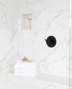 a bathroom with marble walls and white towels on the shelf next to the shower head