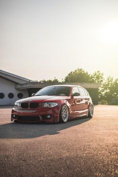 a red car parked in front of a building with the sun shining down on it