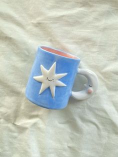 a blue and white coffee cup with a smiling star on it's side sitting on a bed