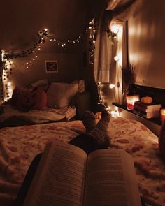 an open book sitting on top of a bed next to a window with fairy lights