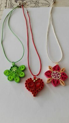 three different necklaces are hanging on a white tablecloth, one is decorated with flowers and the other has an ornament in the shape of a heart