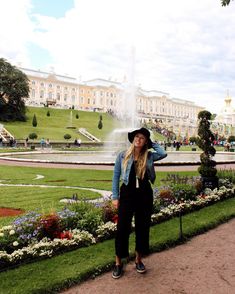 a woman wearing a hat standing in front of a fountain with water spouting from it