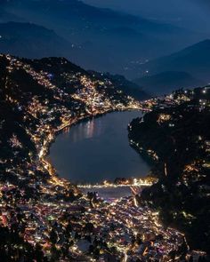 an aerial view of a city at night with lights on the water and mountains in the background