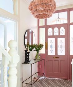 a foyer with pink door, chandelier and mirror on the side walk way