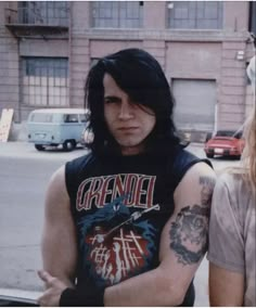 a man with black hair and tattoos on his arm standing in front of a building