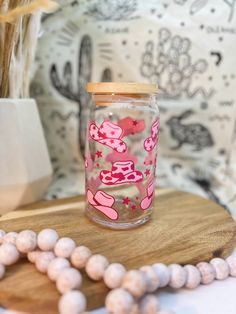 a wooden bead necklace and glass jar with pink designs on it sitting on a table