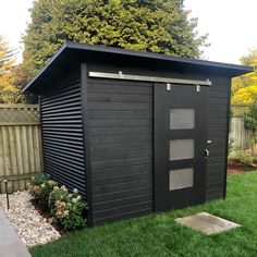 a black shed sitting in the grass next to a fence