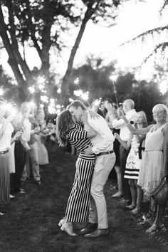 a man and woman kissing while holding sparklers in front of their faces as people look on