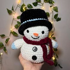 a hand holding a crocheted snowman with a red scarf and black hat