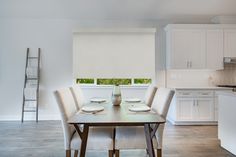 a dining room table and chairs in front of a window with white blinds on the windowsill