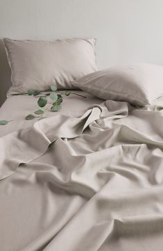 an unmade bed with white sheets and green leaves on the comforter, in front of a white wall