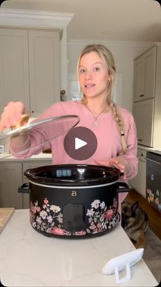 a woman in a pink shirt is holding a spoon over a black crock pot