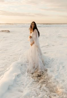 a woman standing in the ocean wearing a white dress