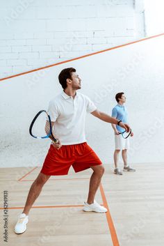 two young men playing tennis in an indoor court, one holding a racket and the other looking up