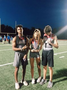 three people standing on a football field with medals around their necks and one person holding a cell phone