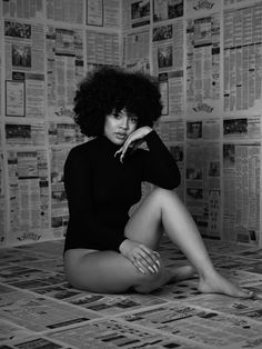 a black and white photo of a woman sitting on the floor in front of newspapers