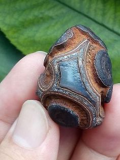 a close up of a person's hand holding a piece of metal in front of a green leaf