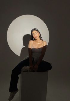 a woman sitting on top of a white block in front of a gray and white circle