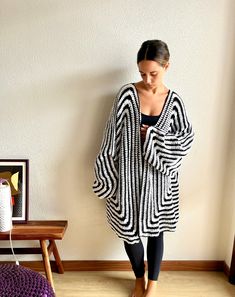 a woman standing in front of a white wall wearing a black and white striped cardigan