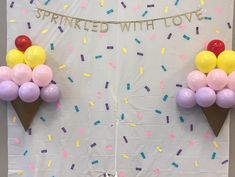 two ice cream cones decorated with balloons and sprinkles on a white wall