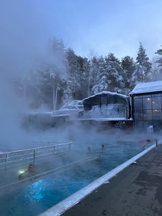 people are swimming in a pool with steam rising from the water and snow on the ground