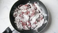 a frying pan filled with powdered sugar covered meat