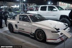 a white sports car is on display at an auto show with other cars in the background