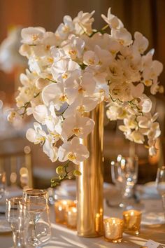 a vase filled with white flowers sitting on top of a table next to glasses and candles