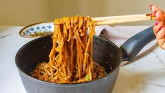 someone is holding chopsticks over some noodles in a pan on the table with other food items